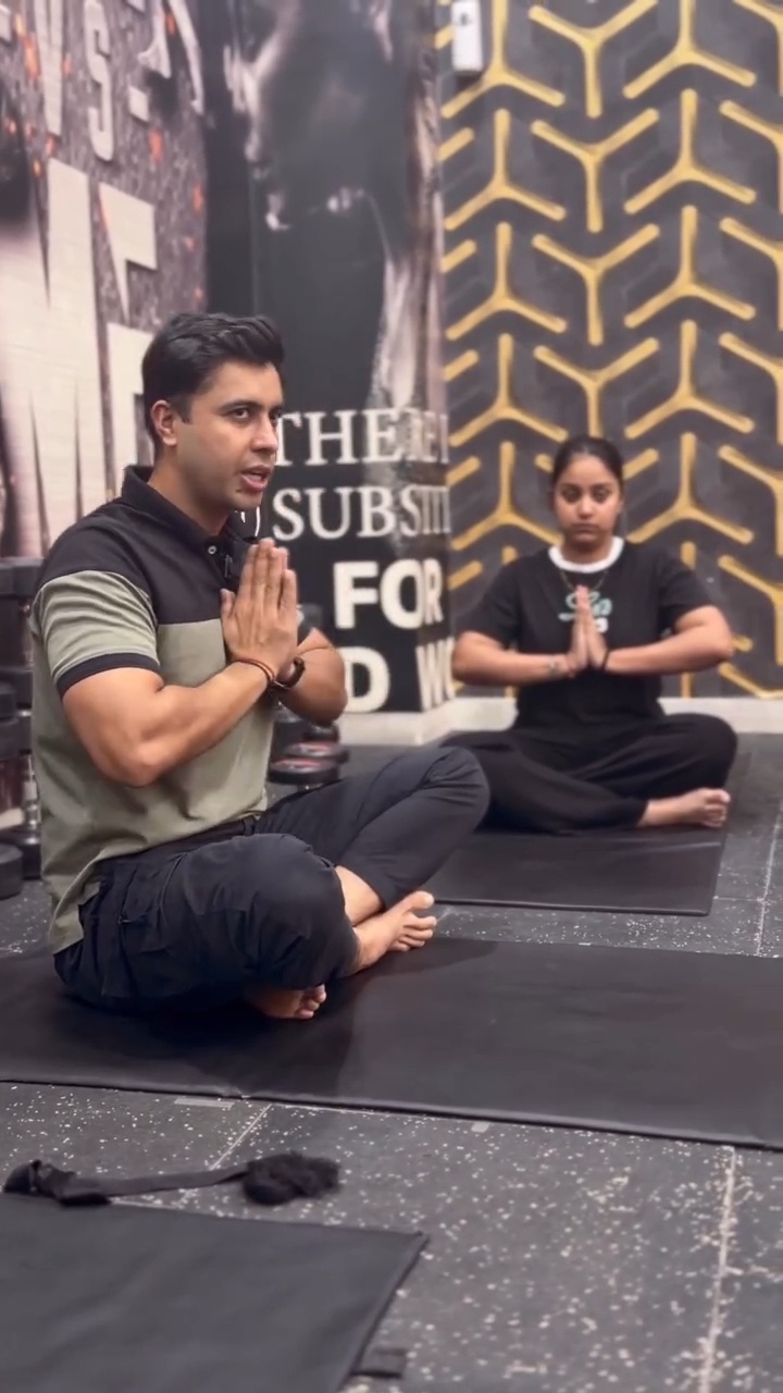 Sumit seated on a mat demonstrating a movement alongside a participant